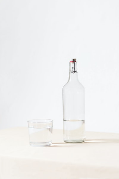 在白色表面的半个空瓶子旁边晃动玻璃